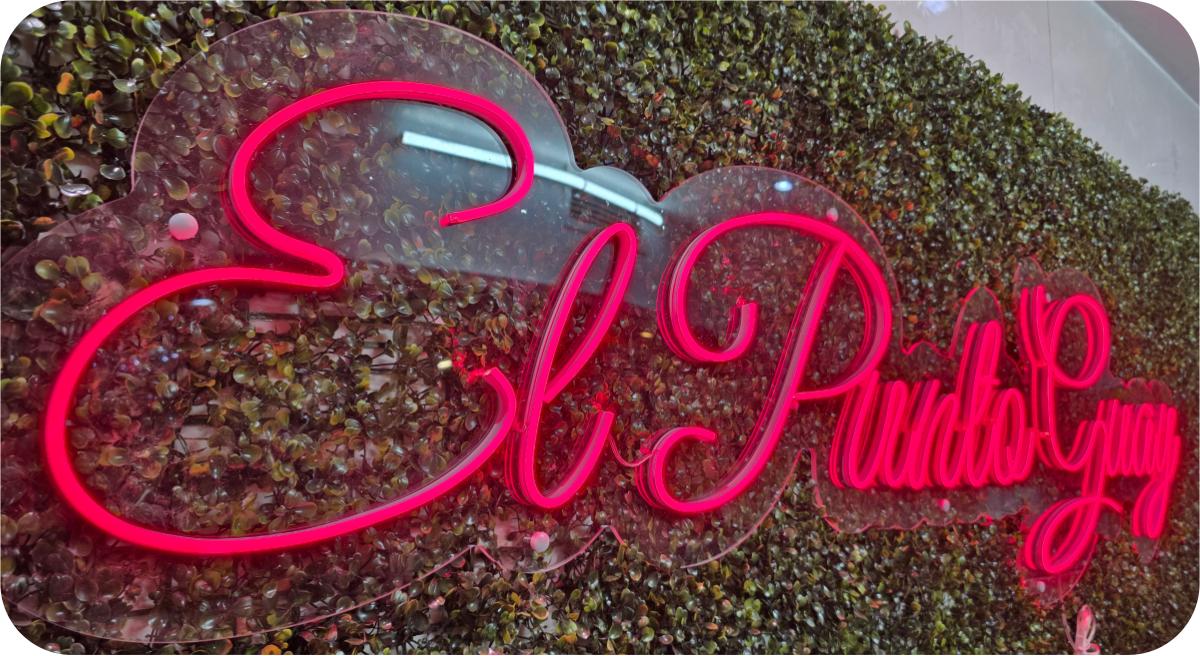 Neón rosa El Punto Guay sobre pared de vegetación con corazón