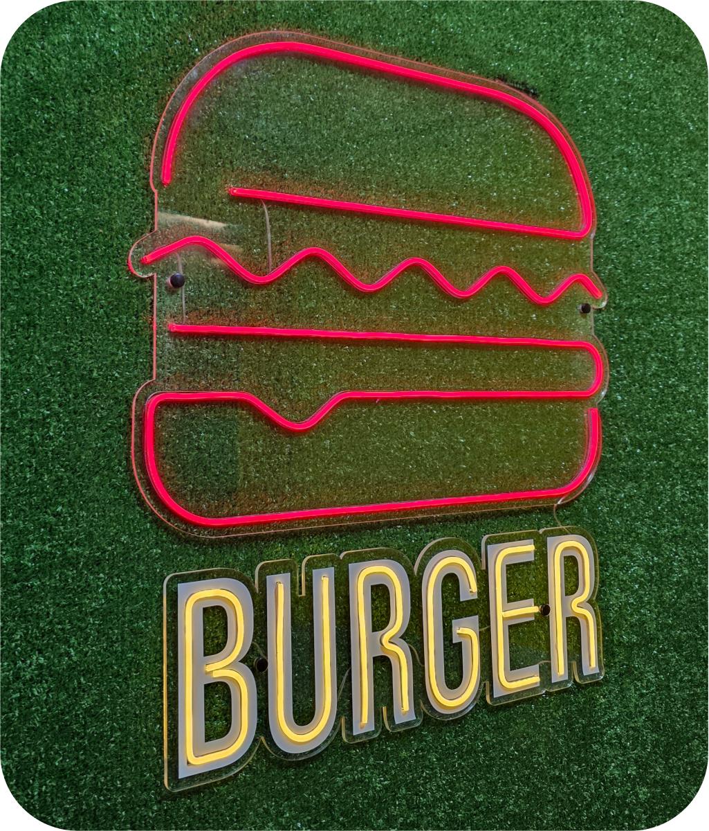 Neón rosa con forma de hamburguesa y texto Burger sobre césped