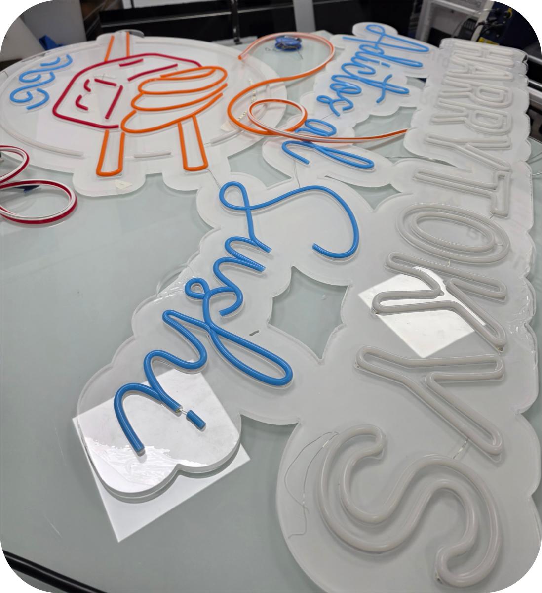 Producción de letreros neón en taller — varios diseños en mesa de trabajo