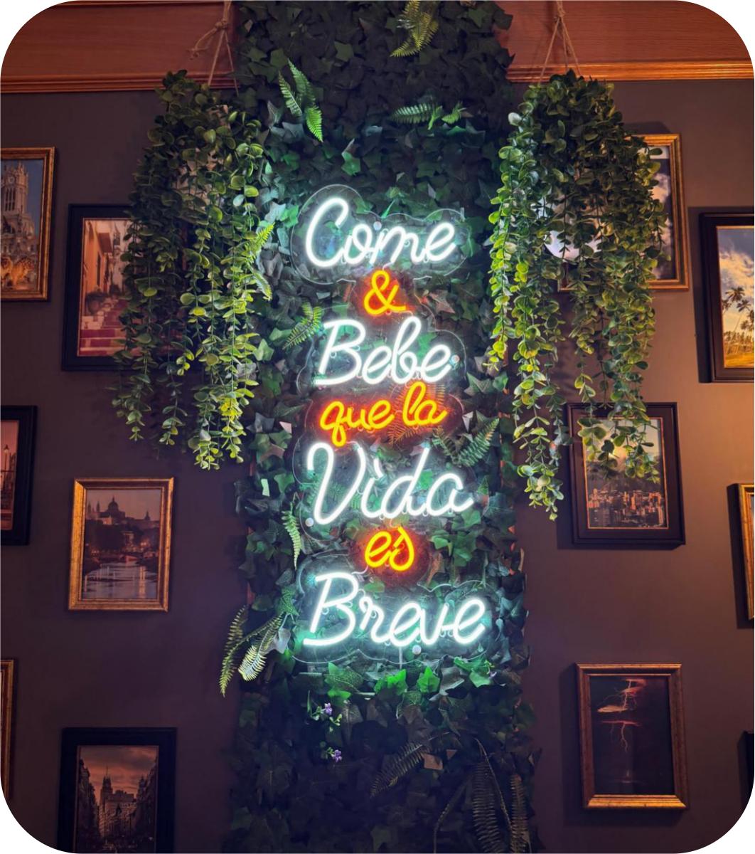 Neón blanco y naranja Come y Bebe que la Vida es Breve con vegetación